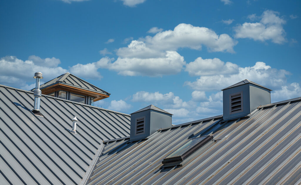 Metal roof with vents, skylights, and chimney under blue sky